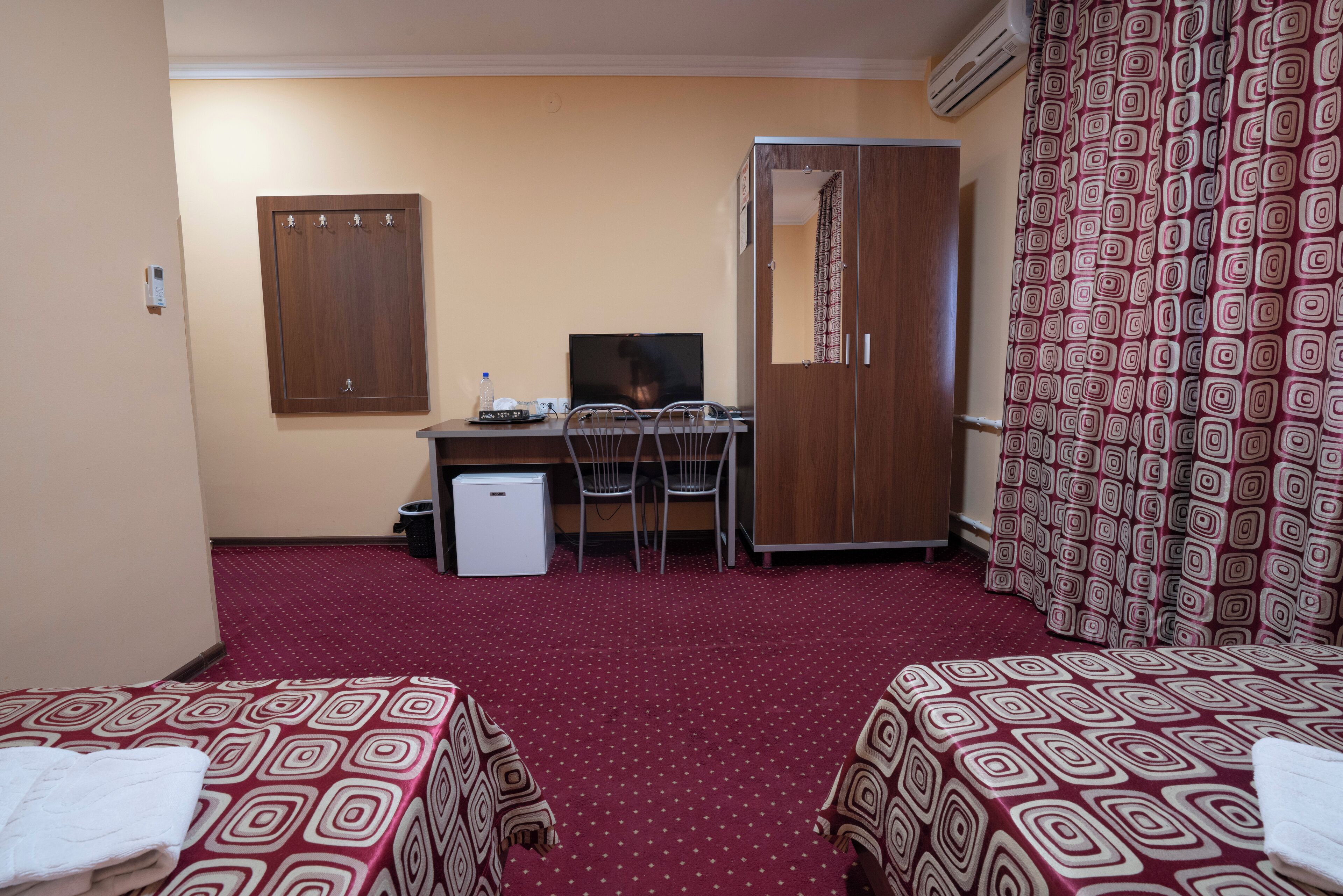 A hotel room with two beds, a desk with a chair, a television, and a wardrobe.