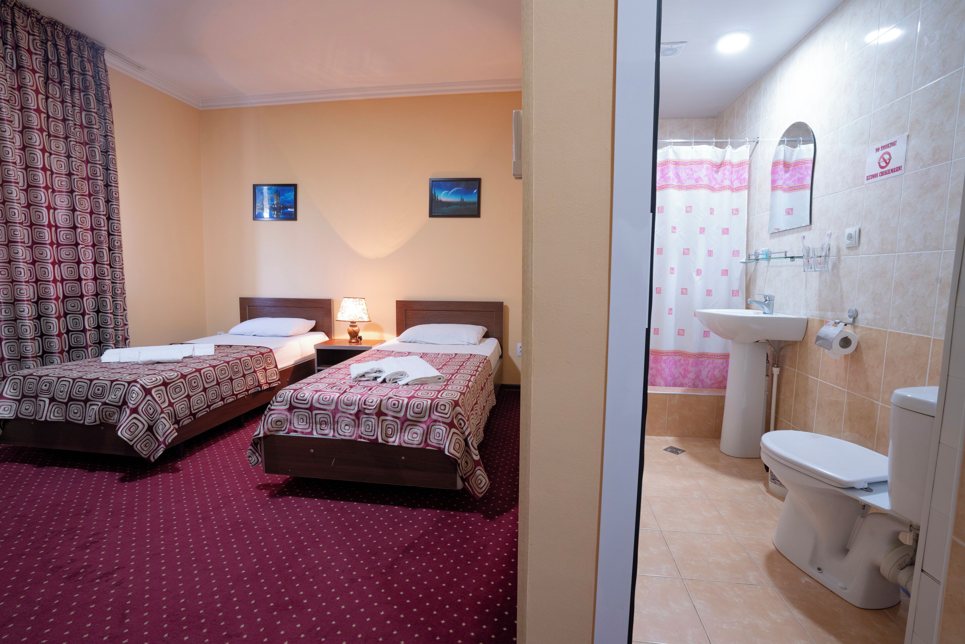 A hotel room with two beds, a nightstand, a lamp, a bathroom with a toilet, sink, and mirror.