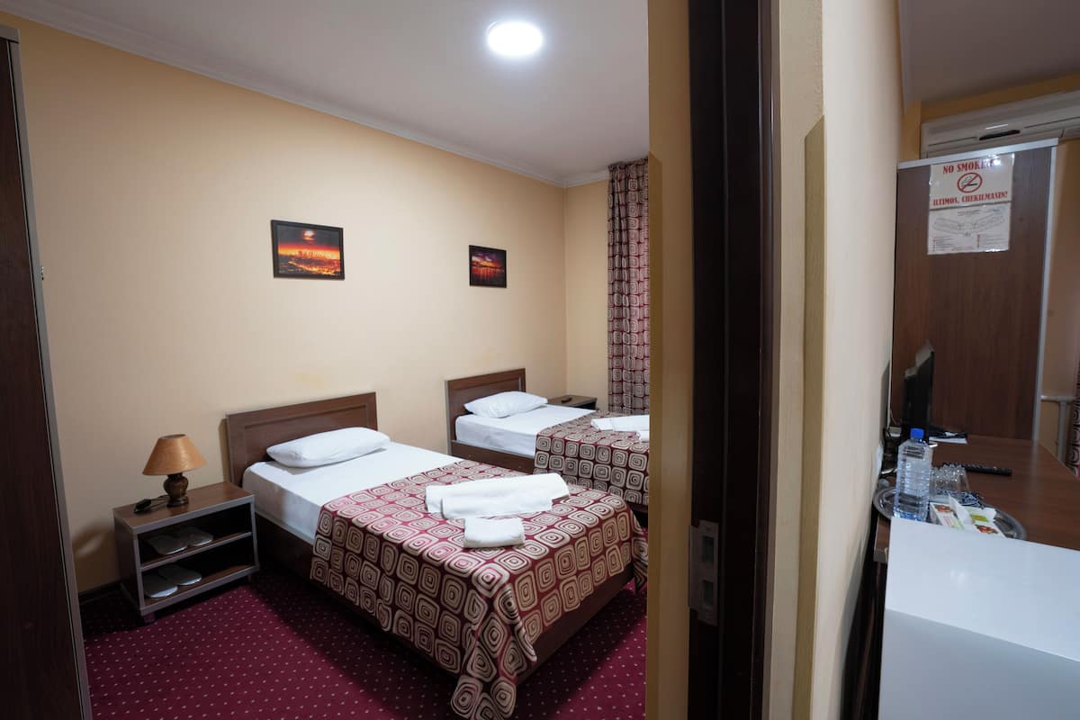 A hotel room with two beds, a nightstand, a lamp, and a bathroom with a towel rack.