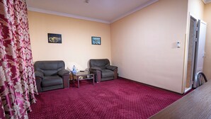 A room with two leather chairs, a small table, a red carpet, and two framed pictures on the wall. - Rohat Hotel (Tashkent)