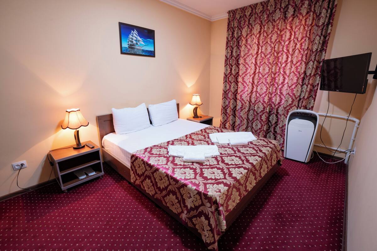 A hotel room with a bed, two bedside lamps, a television, and a small desk with a lamp.