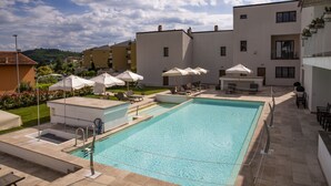 En swimmingpool med liggestole og parasoller, omgivet af bygninger.