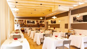 En restaurant med flere borde dækket til spisning, hvide duge og et udvalg af vinflasker på væggene.