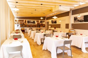 Restaurante com várias mesas preparadas para refeições, com toalhas brancas e diversos vinhos expostos nas paredes.