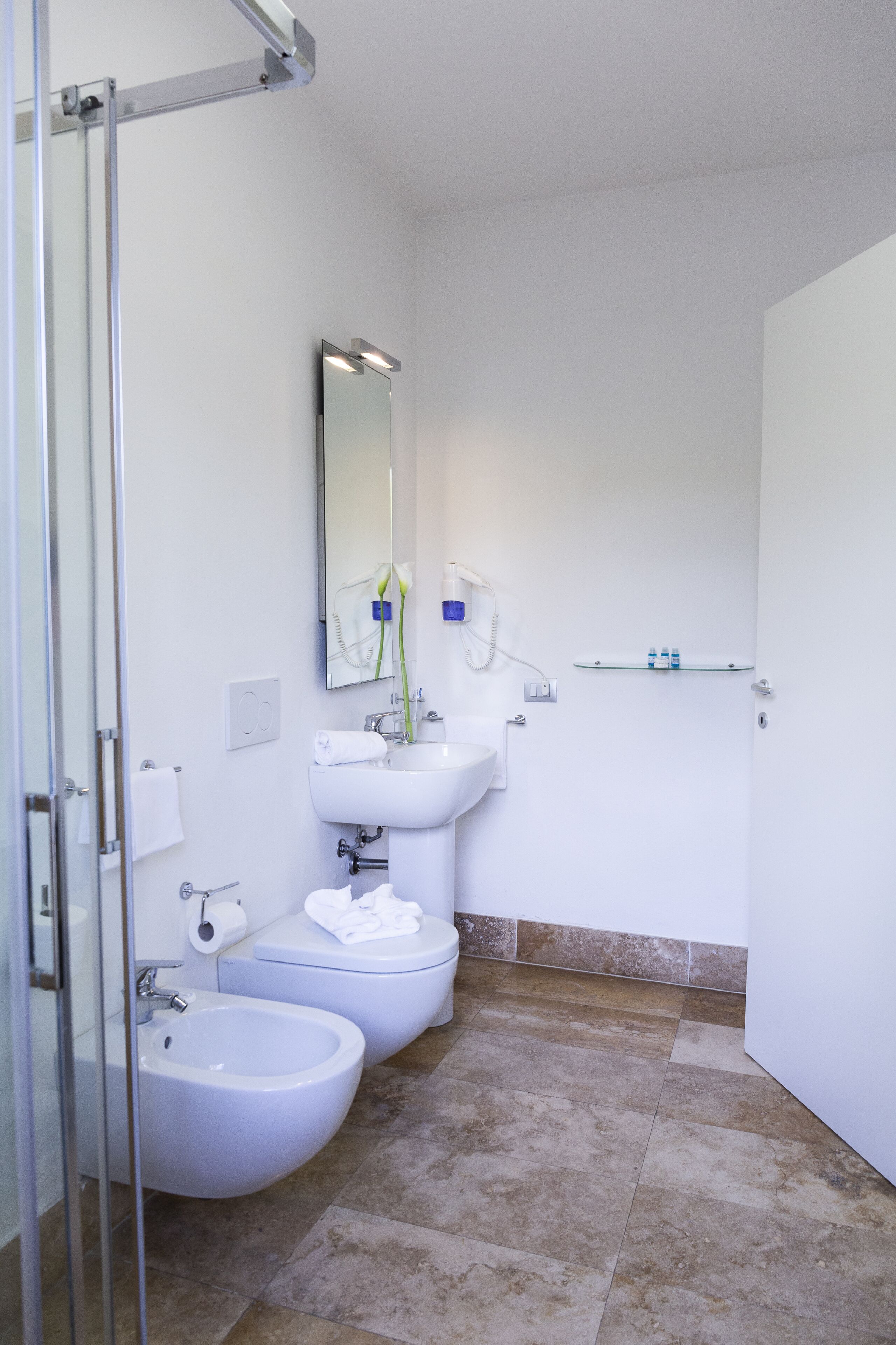 A bathroom with a toilet, bidet, sink, and a glass shower enclosure.