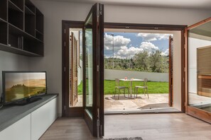 A modern living room with a television, a sliding glass door leading to a patio with outdoor furniture. - The Florence Hills Resort & Wellness (Pelago)