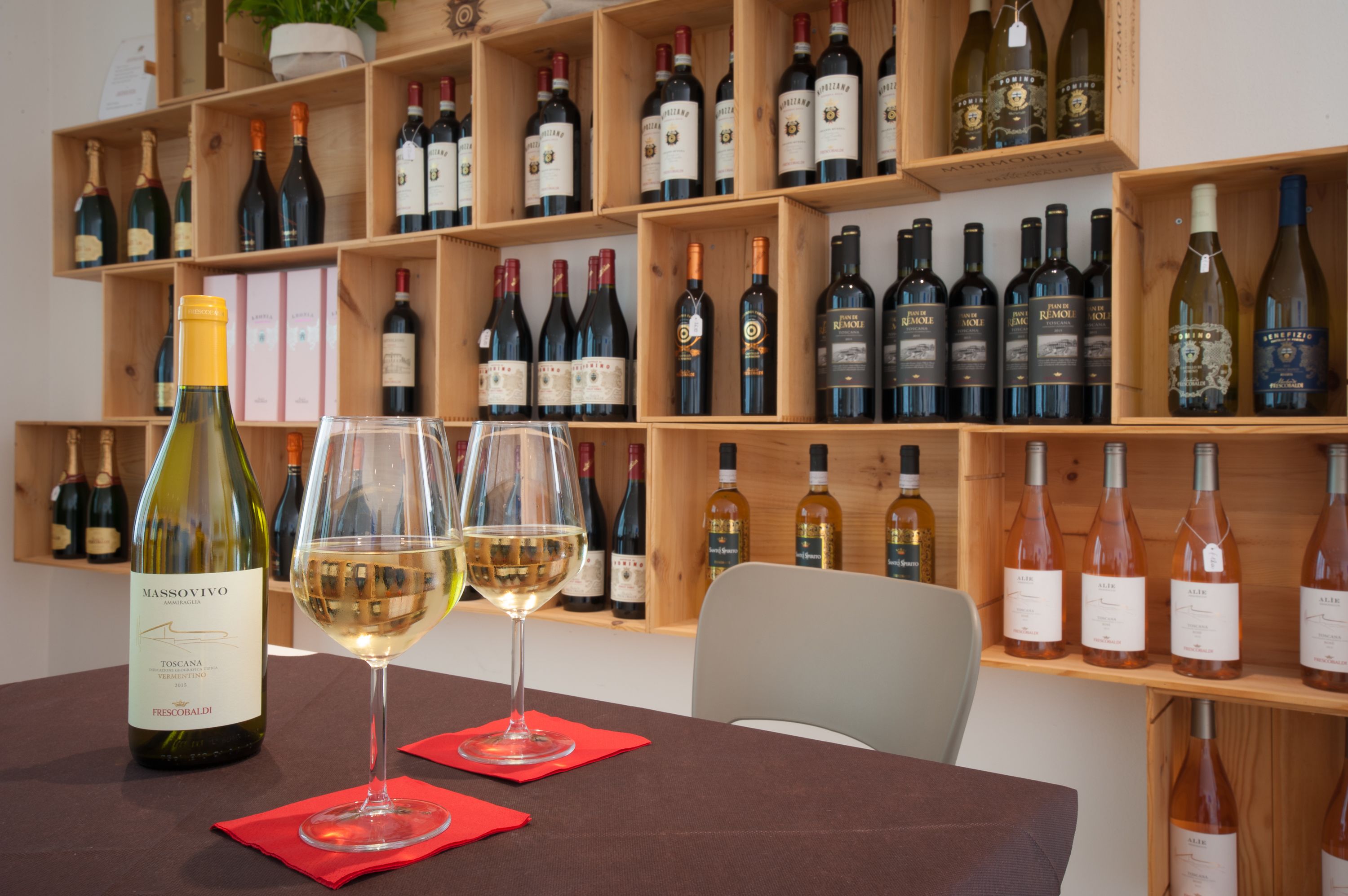A wine tasting room with a wooden wine rack filled with various bottles. Two wine glasses are on a table in front of the rack.