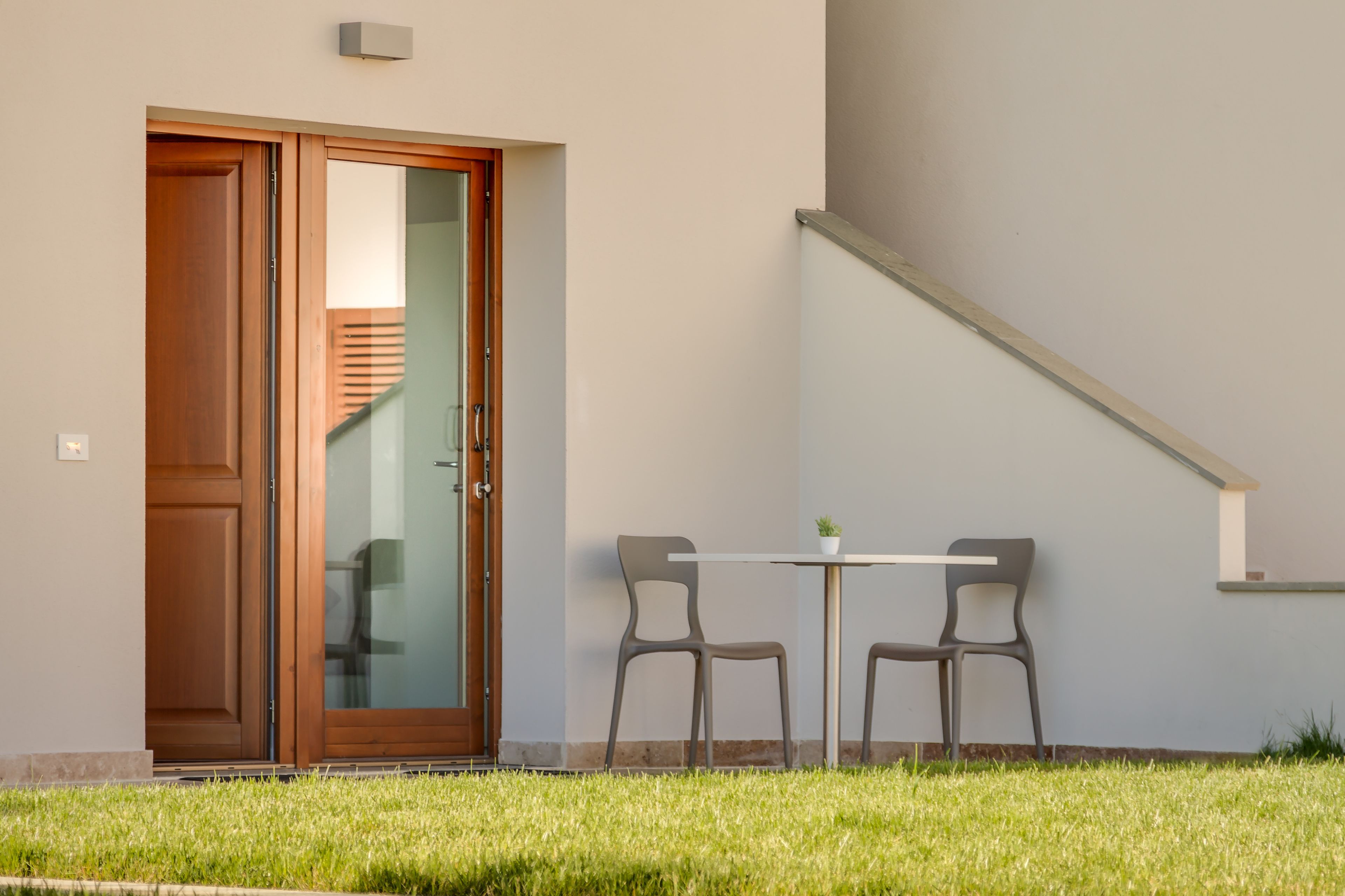 Un edificio moderno con una puerta de madera, una pequeña mesa con dos sillas y una escalera.