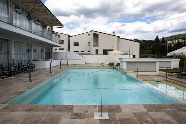 A swimming pool with a rope barrier, outdoor seating, and a building with multiple windows and balconies. - The Florence Hills Resort & Wellness (Pelago)