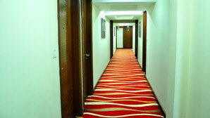 A hotel hallway with a red and white striped carpet, wooden doors, and framed pictures on the walls. - Hotel Jewel Palace (New Delhi)
