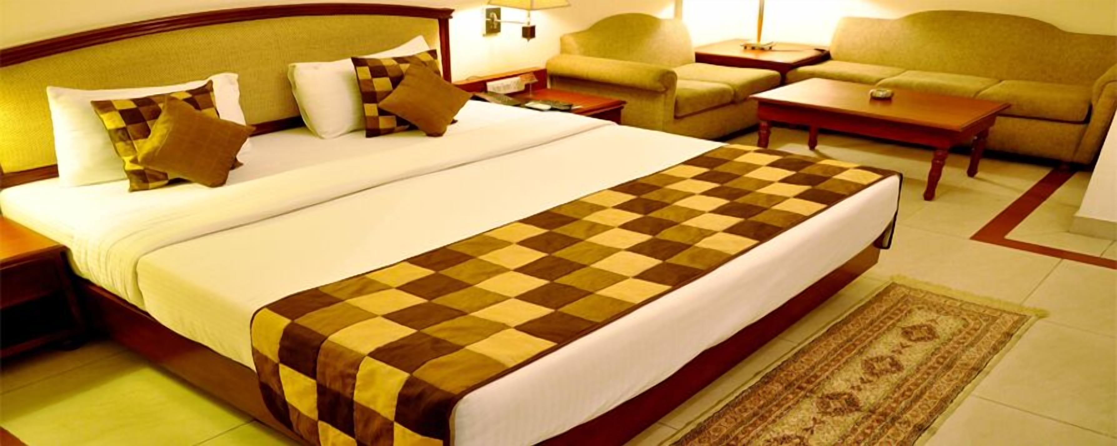 A hotel room with a large bed, a sofa, a coffee table, and a patterned rug.