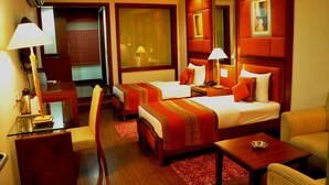 A hotel room with two beds, a desk, a chair, and a small table. - Hotel Jewel Palace (New Delhi)