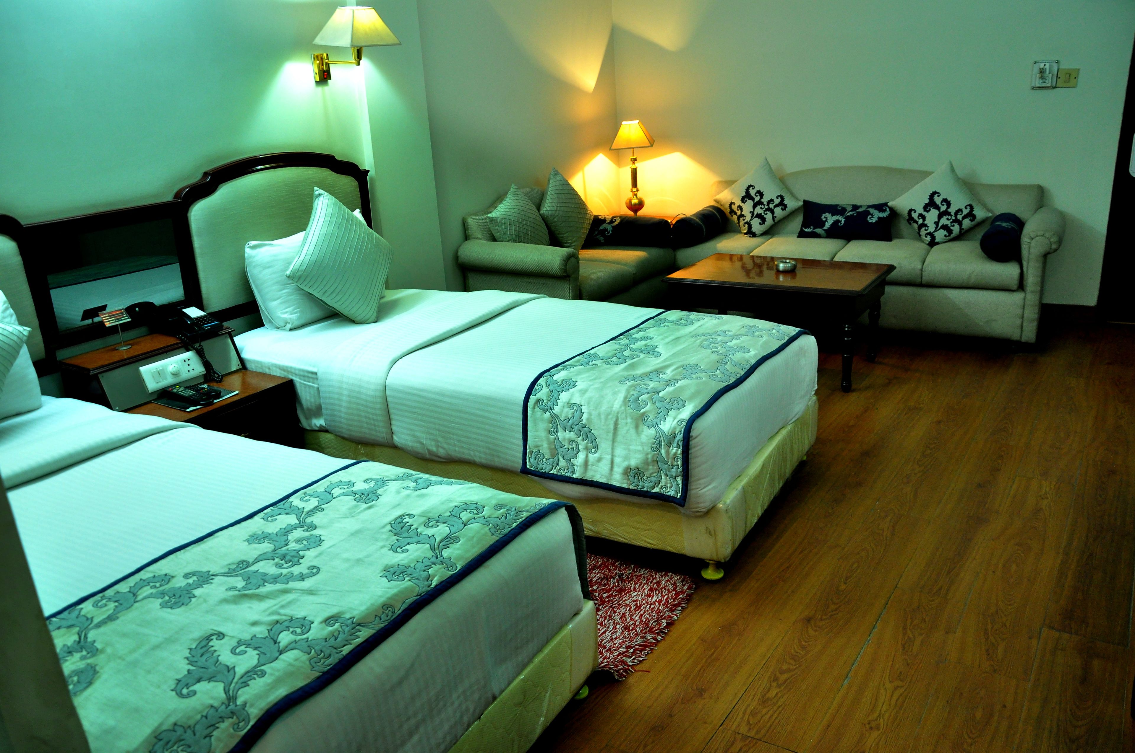 Habitación de hotel con dos camas, un sofá, una mesita y una lámpara.