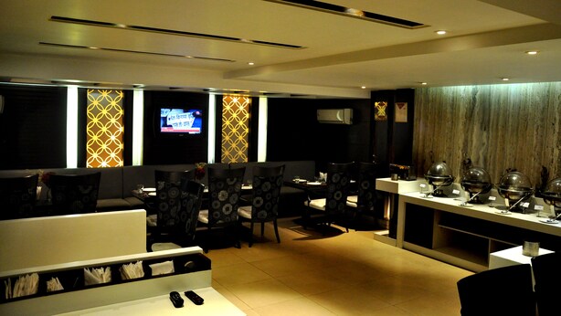 A modern restaurant with a long counter, multiple seating areas, and a television screen. - Hotel Jewel Palace (New Delhi)