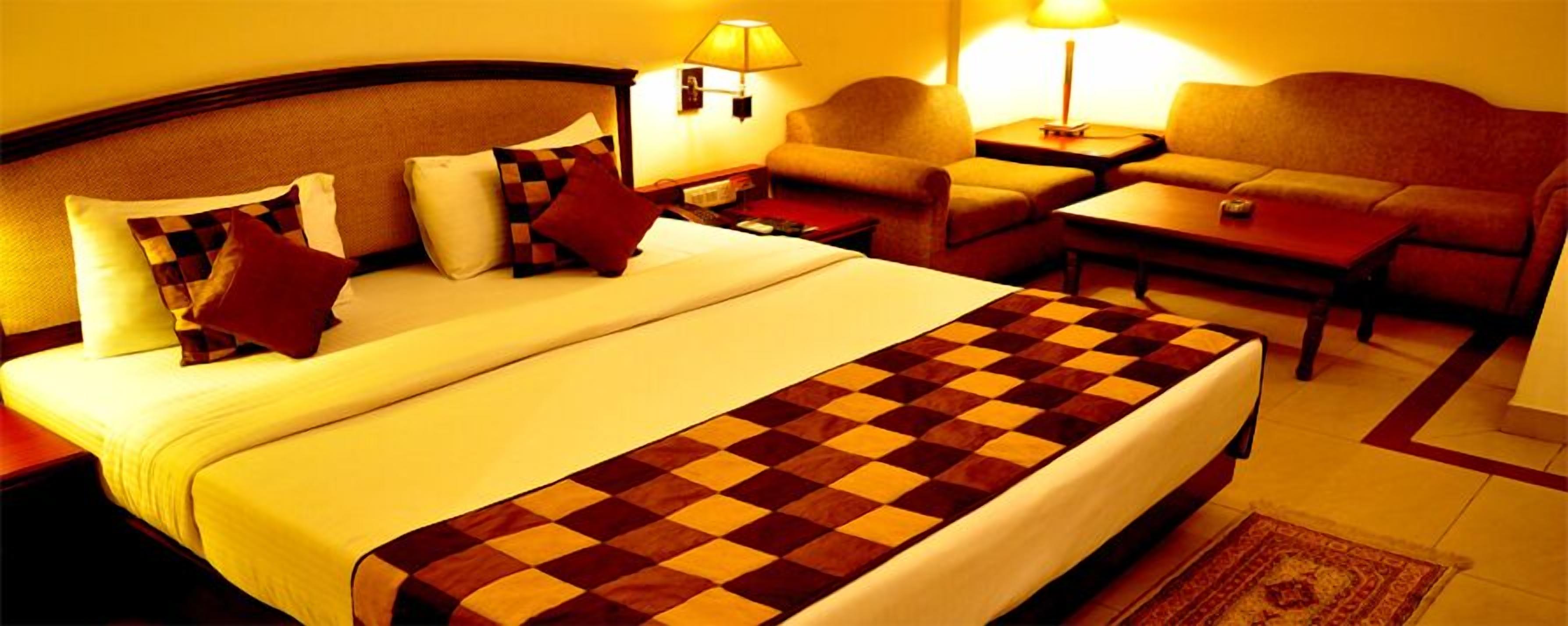 A hotel room with a large bed, a sofa, a small table, and two lamps.