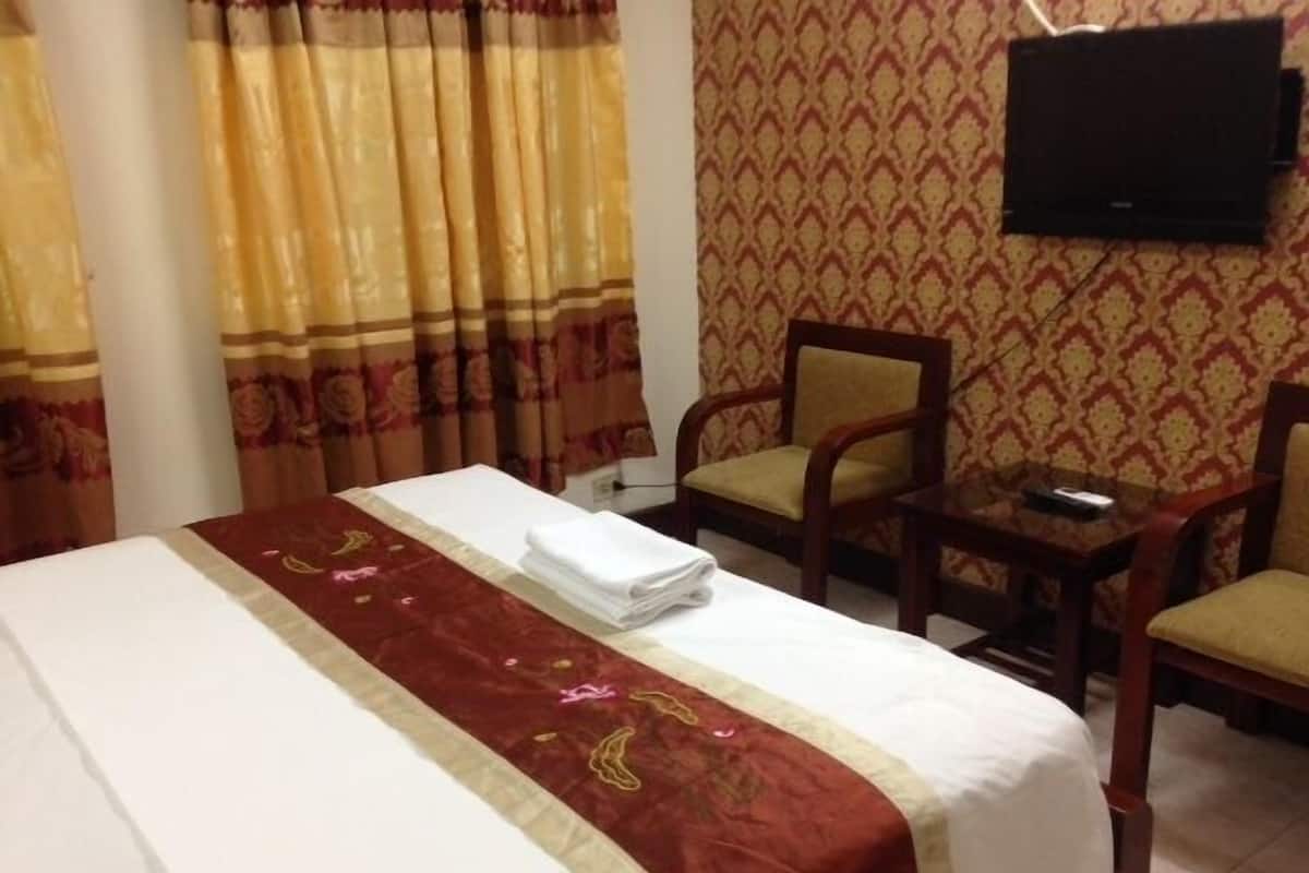 A hotel room with a neatly made bed, a chair, a small table, and a television mounted on the wall.