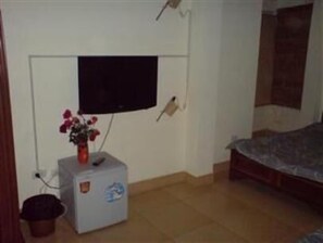 A small room with a bed, a television mounted on the wall, a small fridge, and a flower vase.