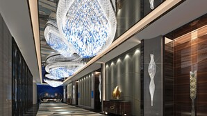 A modern hotel corridor with a patterned carpet, large decorative ceiling lights, and a view of the cityscape. - Wanda Realm Changzhou (Changzhou)