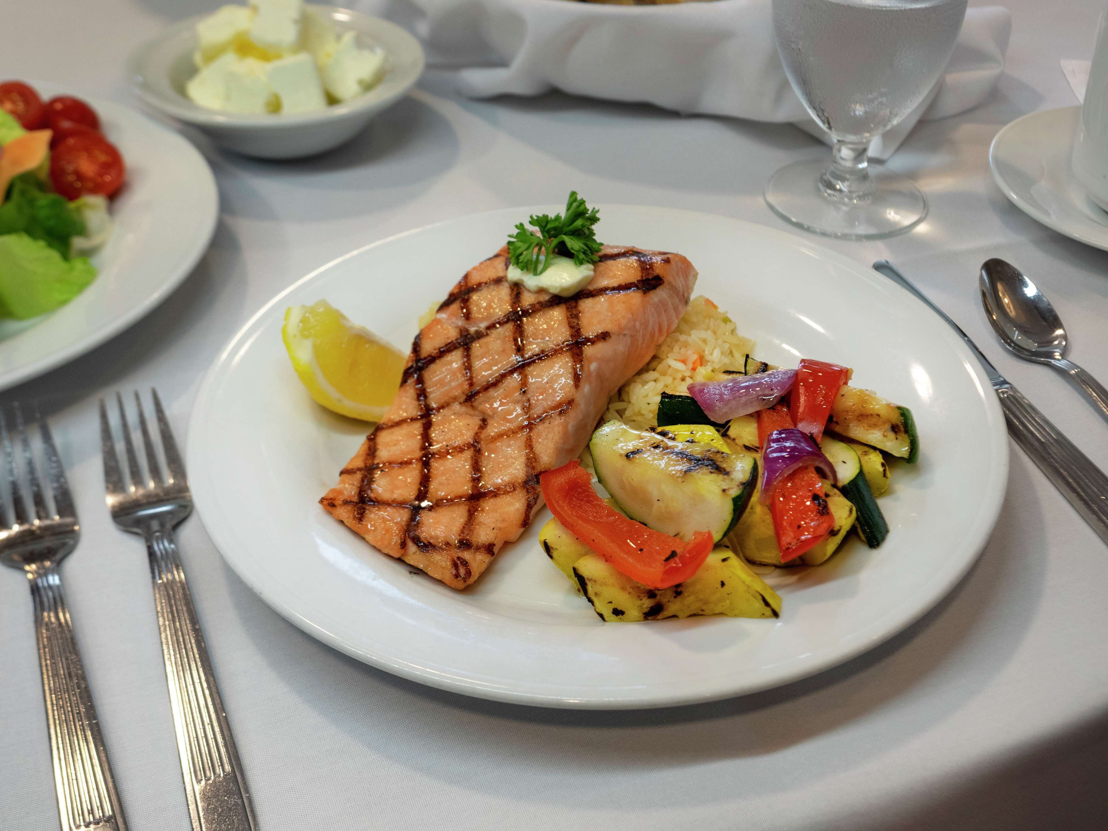 A plate of grilled salmon with vegetables and a lemon wedge.