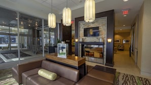 A modern lobby with a leather sofa, a fireplace, and a television mounted on the wall. - Hilton Garden Inn Buffalo Downtown (Buffalo)