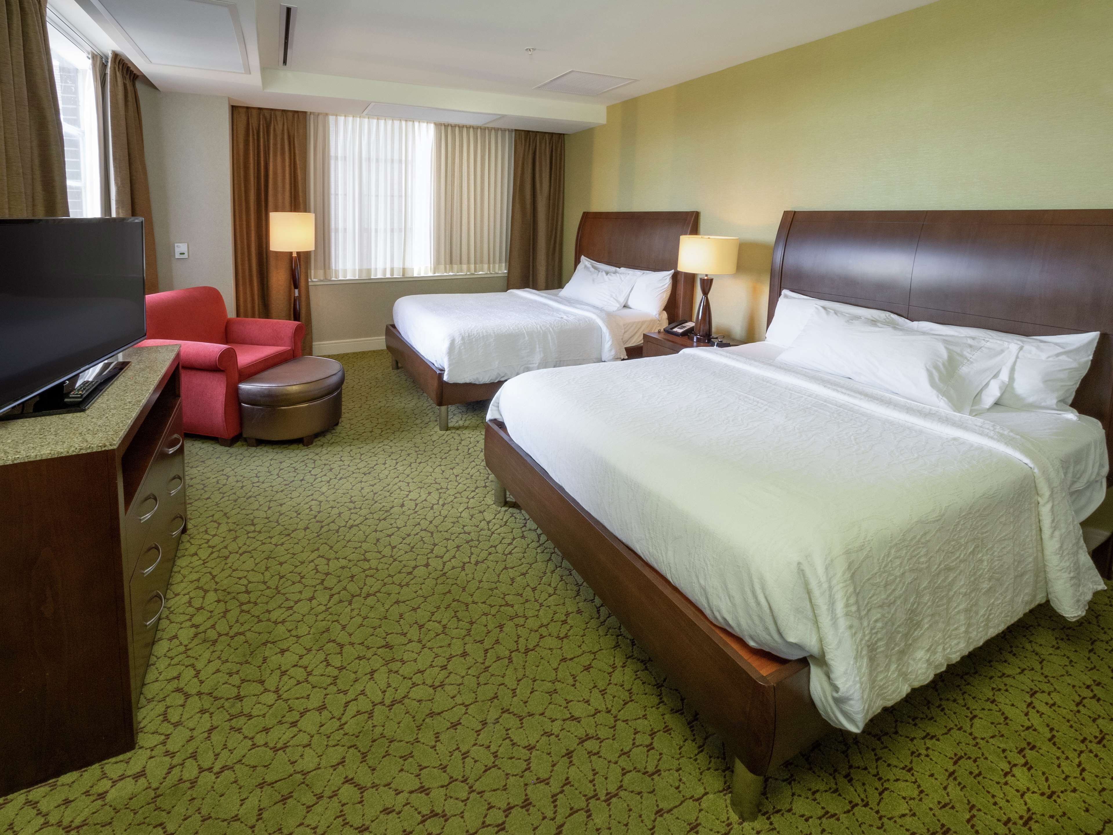 Une chambre d’hôtel avec deux lits, une télévision, un bureau et une chaise rouge.