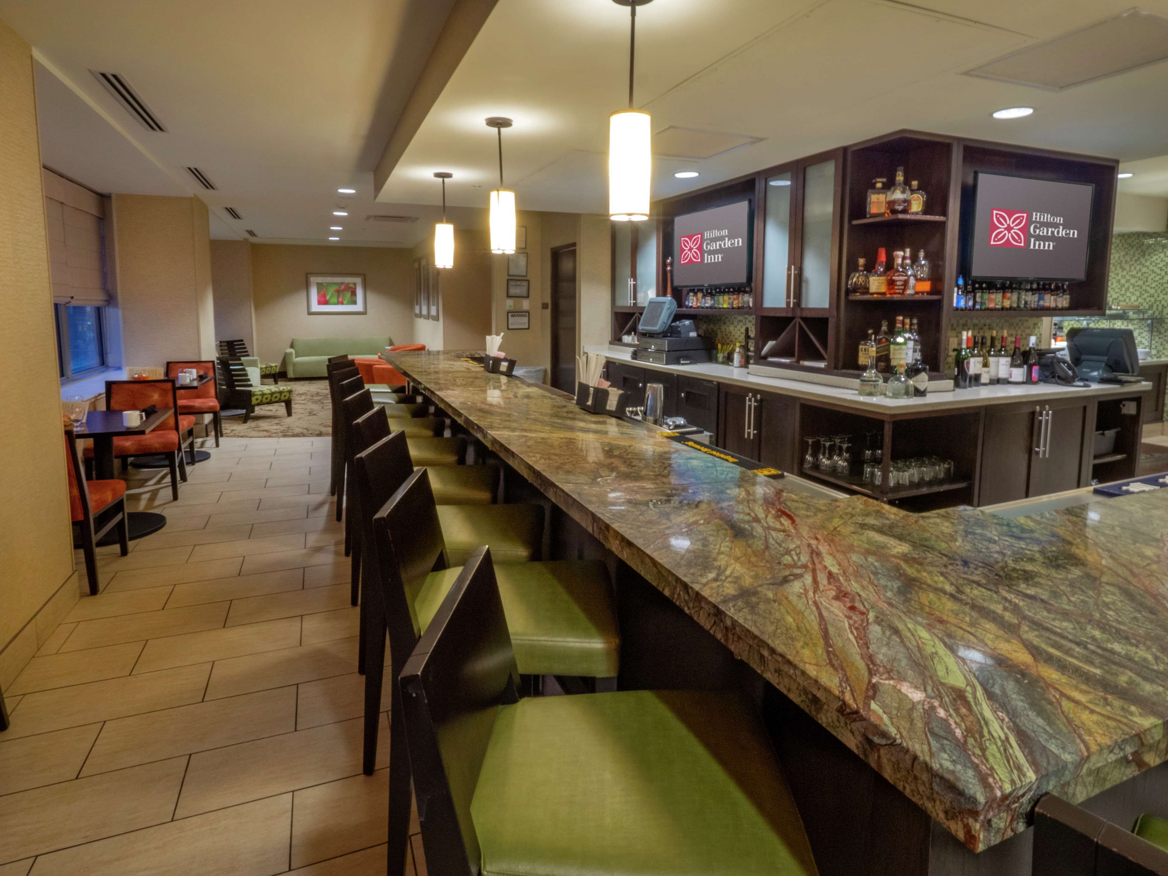 A hotel bar with a long counter, bar stools, and a seating area with couches and chairs.