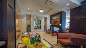 A lobby area with a reception desk, seating arrangements, a coffee station with beverages and snacks, and a decorative wall with a fireplace. - Hilton Garden Inn Buffalo Downtown (Buffalo)