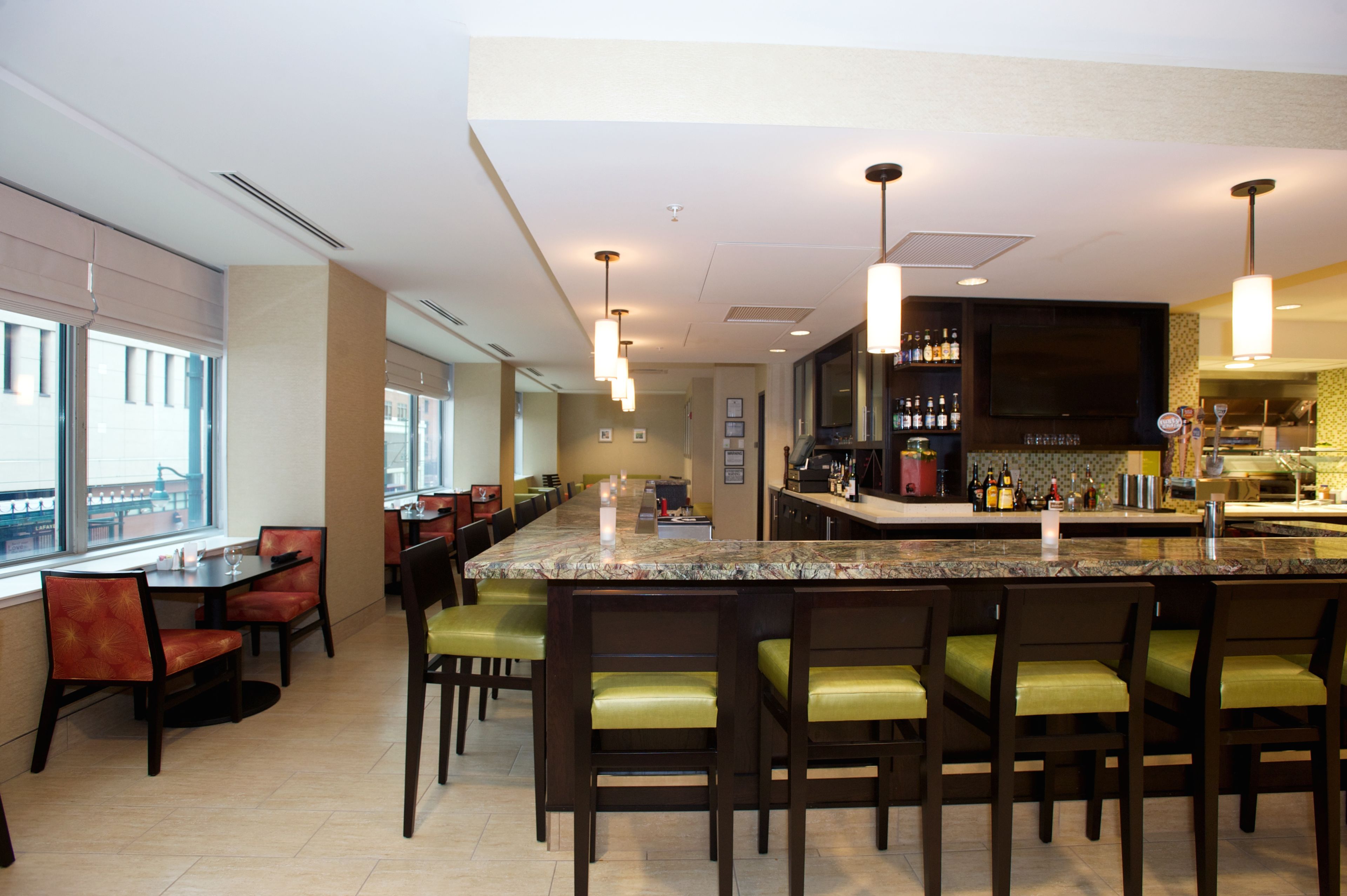 Un restaurante moderno con zona de bar, sillas con asientos acolchados verdes y una larga mesa de comedor.