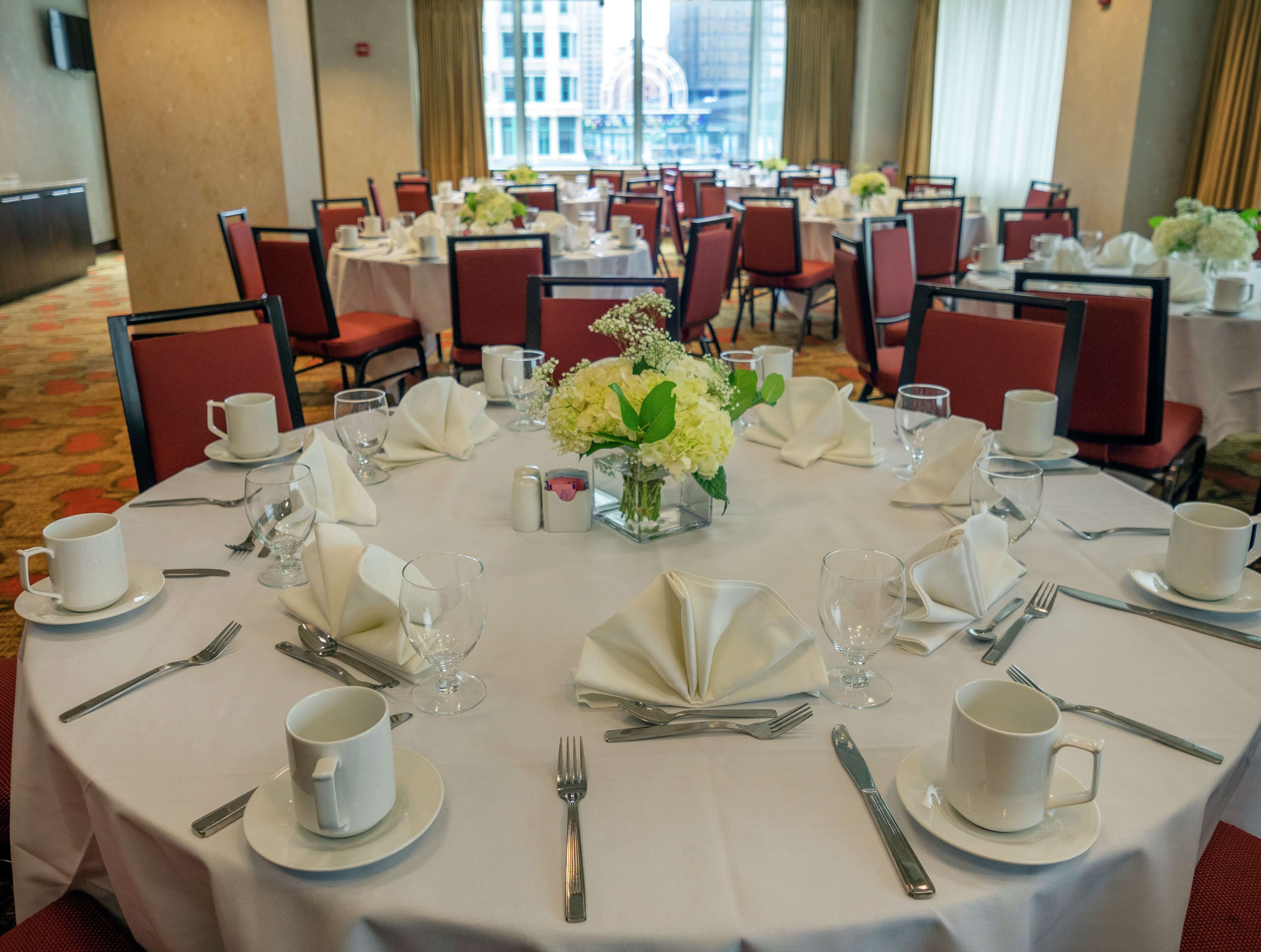 Un salón de banquetes con mesas redondas dispuestas para comer, con manteles blancos, cubiertos y centros de mesa florales.