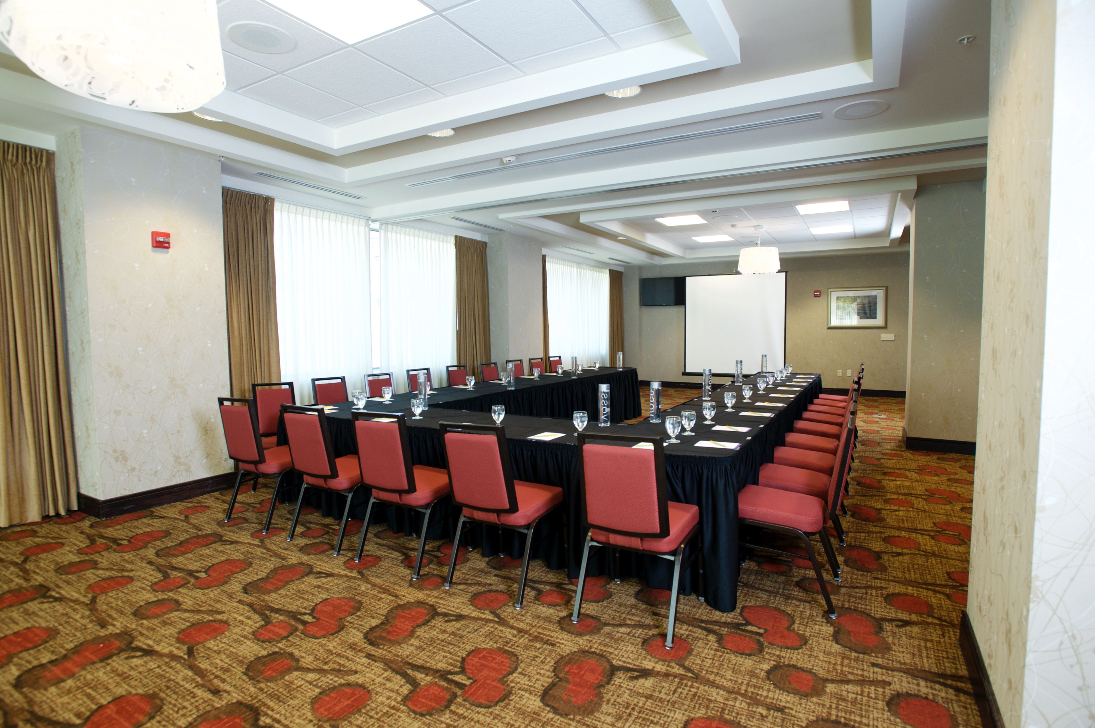 A conference room with a long table, red chairs, and a patterned carpet.