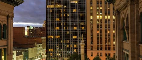 Un hôtel Hilton Garden Inn doté d’une façade moderne en verre, entouré de bâtiments historiques et bordé d’une rue animée, le tout baigné par la lumière du crépuscule.