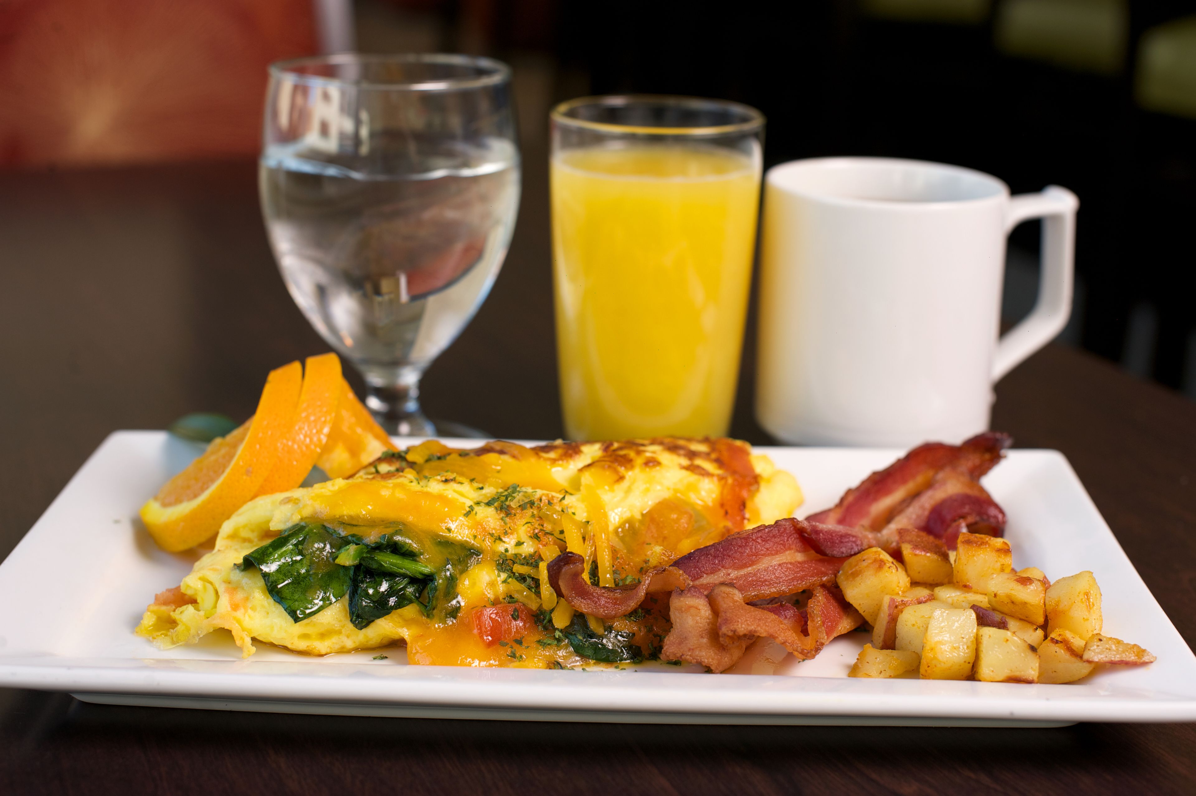 A breakfast plate with eggs, bacon, potatoes, an orange slice, and a glass of orange juice.