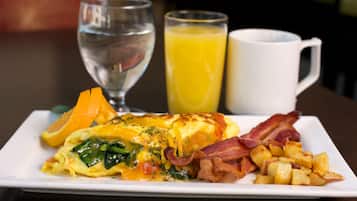 A breakfast plate with eggs, bacon, potatoes, an orange slice, and a glass of orange juice.