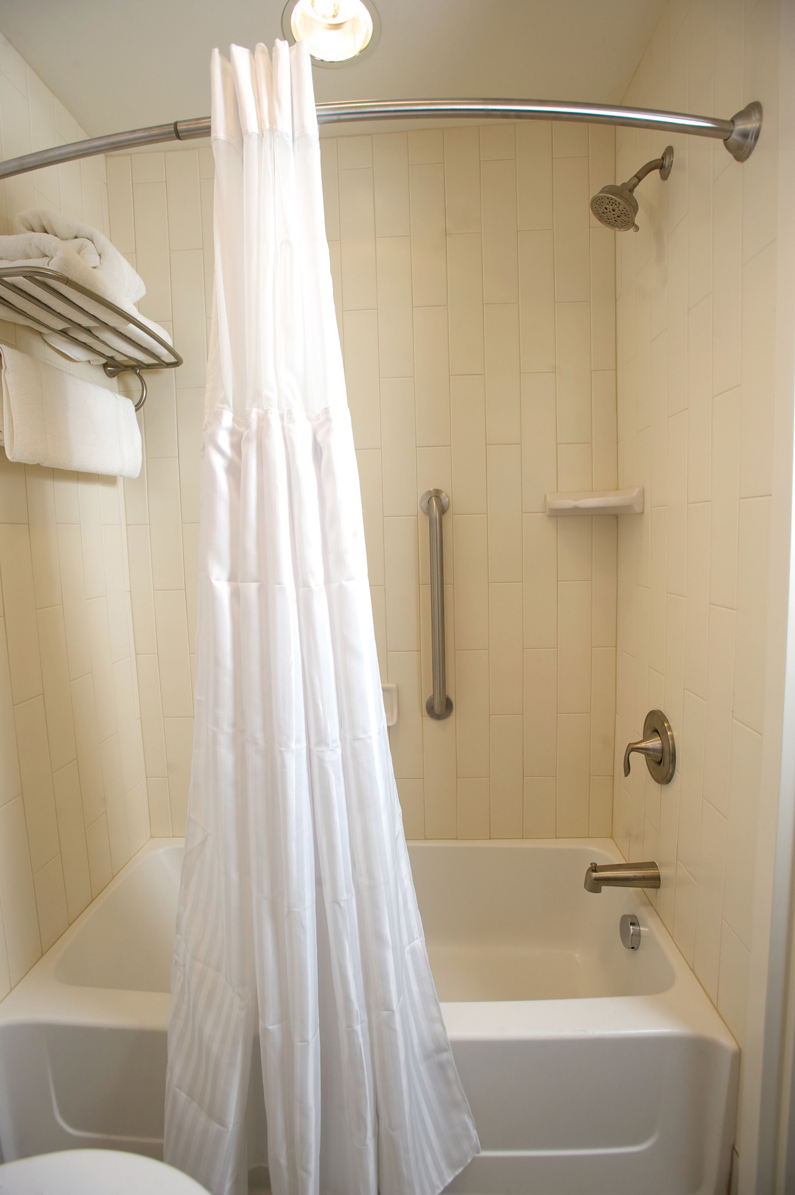 A bathroom with a bathtub, a showerhead, and a handrail.