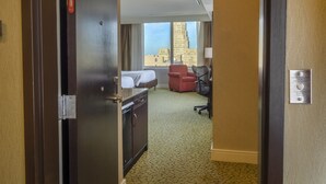 A hotel room with a bed, a desk, a chair, and a view of a cityscape through large windows. - Hilton Garden Inn Buffalo Downtown (Buffalo)