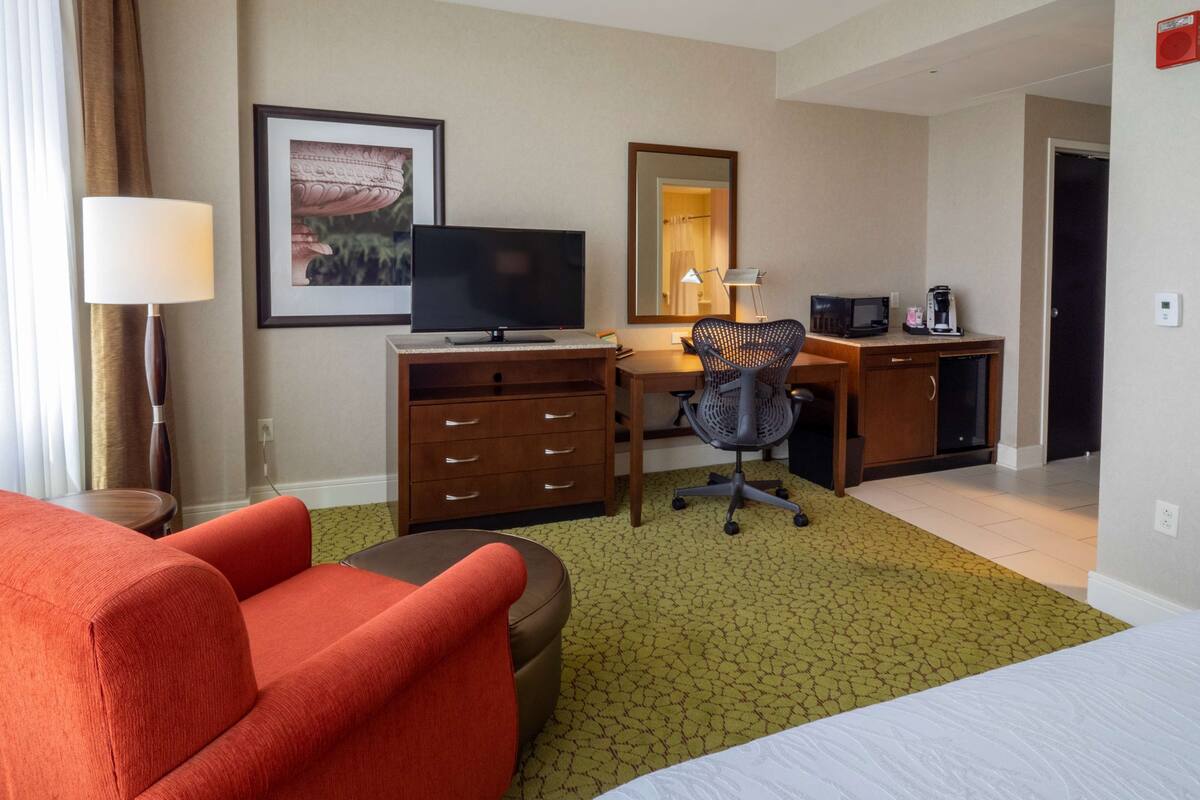 Une chambre d’hôtel équipée d’un lit, d’un bureau avec un ordinateur, d’une chaise, d’une télévision, d’une machine à café et d’un tableau encadré au mur.