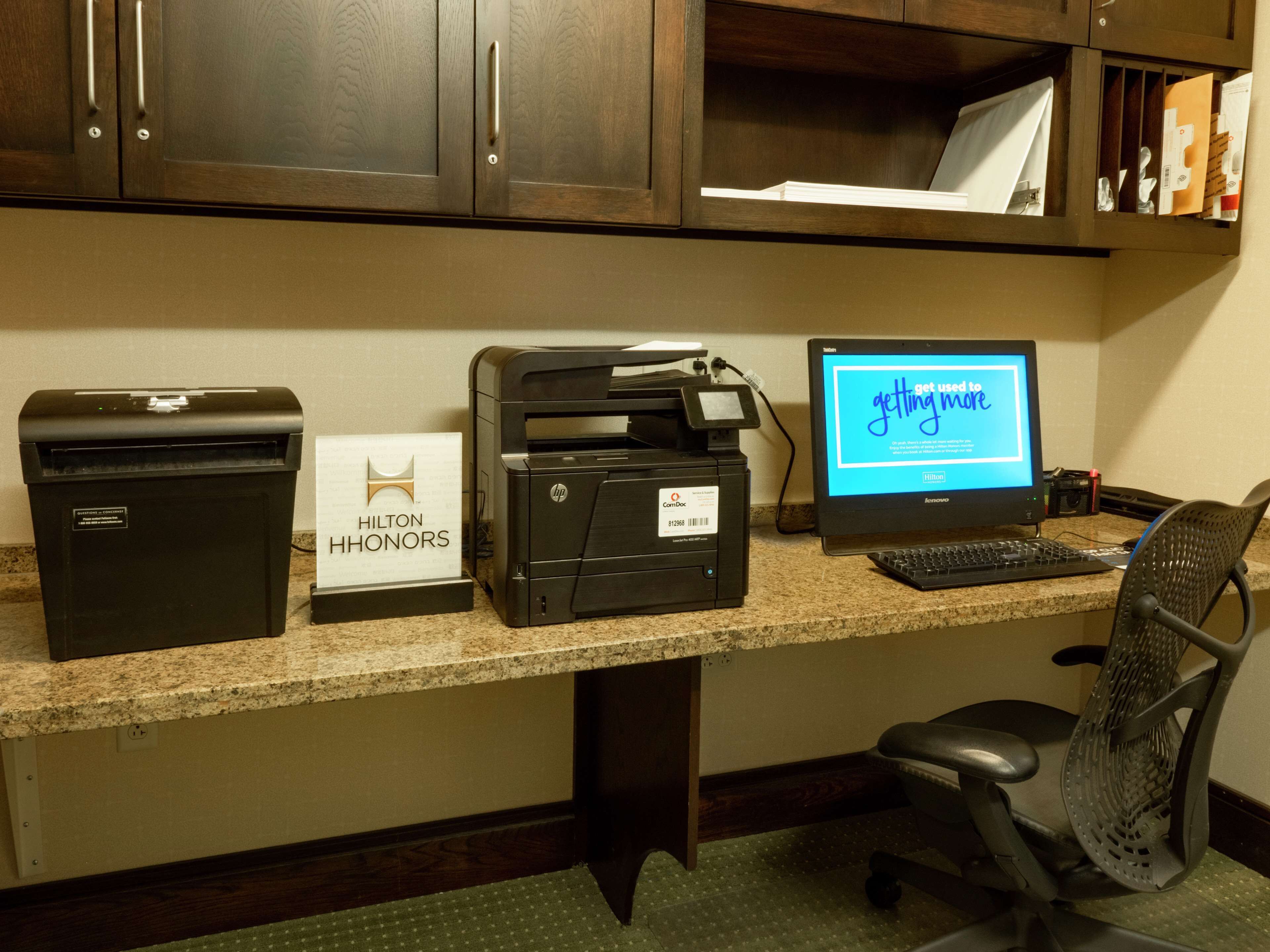 A hotel office with a printer, a computer monitor displaying a message, and a trash bin labeled "Hilton Honors".