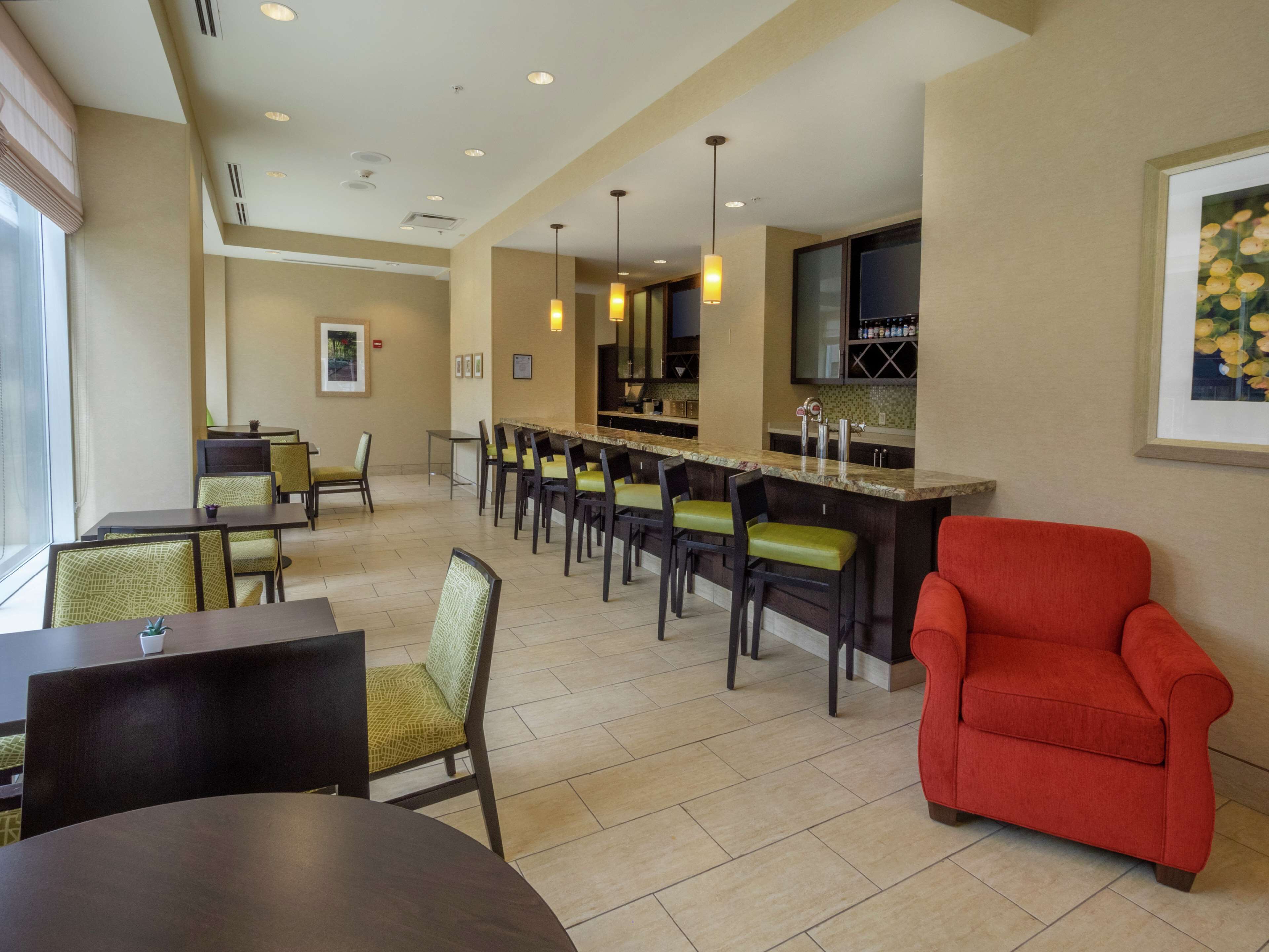 A hotel lobby with a bar area, seating arrangements, and a large window providing natural light.