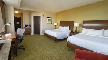 A hotel room with two beds, a desk, a chair, a desk lamp, a telephone, and a coffee maker.