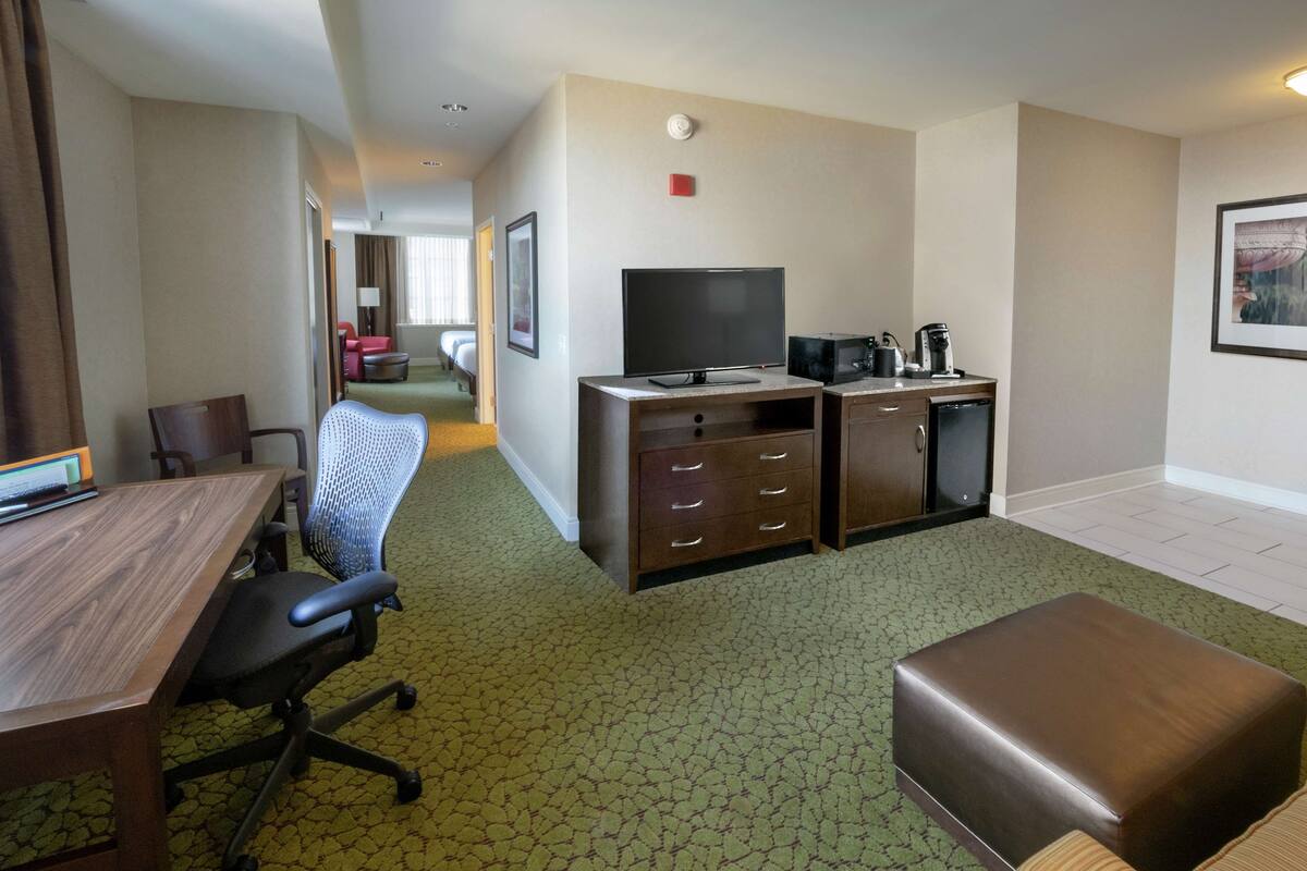 Une chambre d’hôtel équipée d’un bureau en bois, d’un fauteuil de bureau, d’une kitchenette, d’une télévision et d’un lit.
