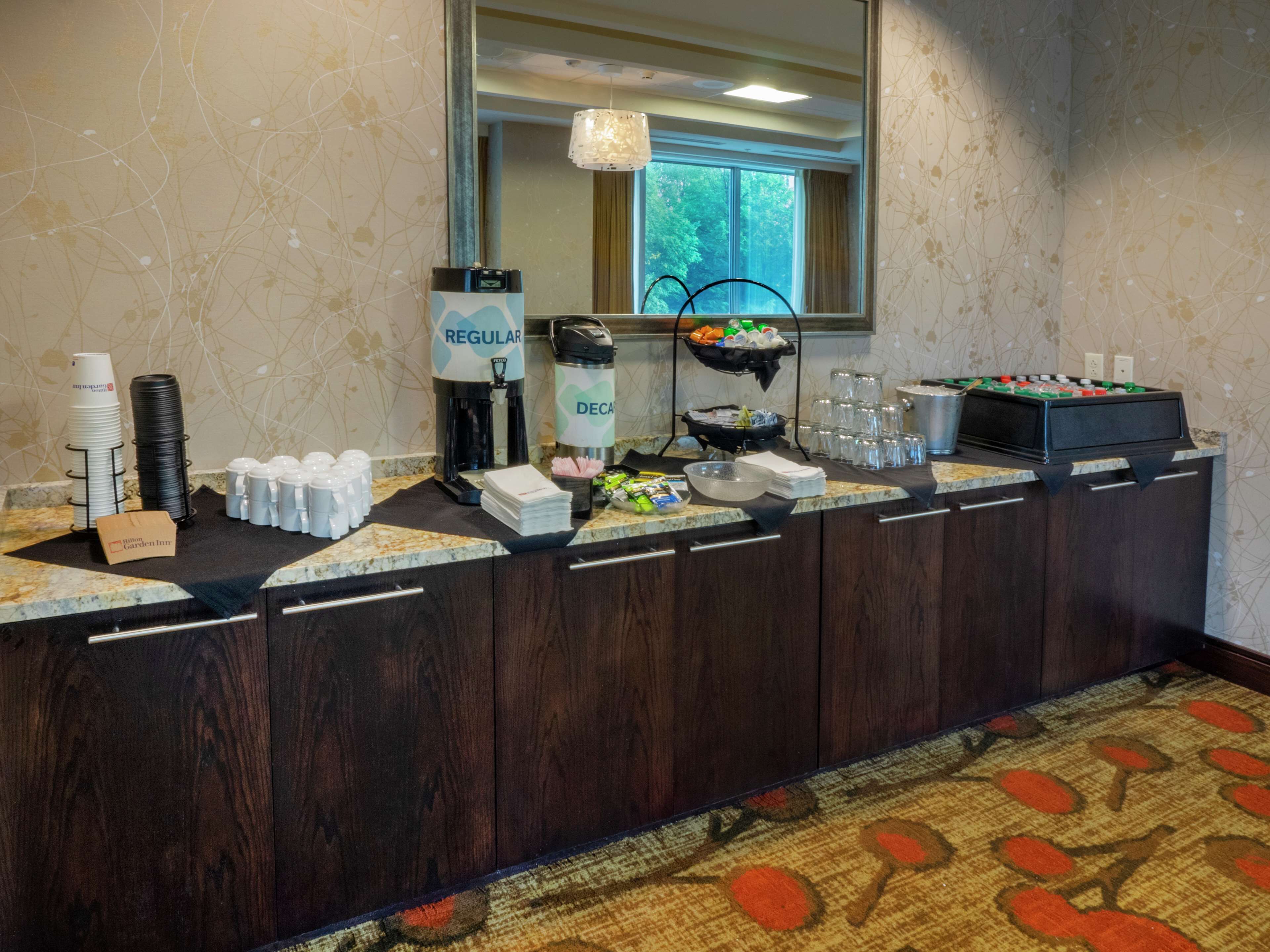 A hotel reception area with a coffee station, a refrigerator, and a window with a view of trees.