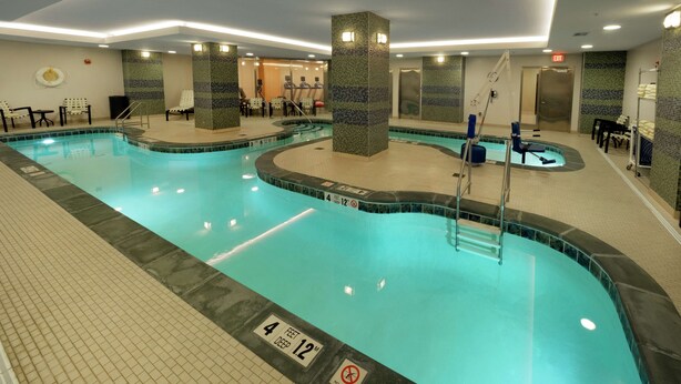 An indoor swimming pool with tiled walls, a lifeguard chair, and a pool ladder. - Hilton Garden Inn Buffalo Downtown (Buffalo)