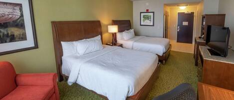 A hotel room with two beds, a desk, a TV, a chair, and a framed picture on the wall.