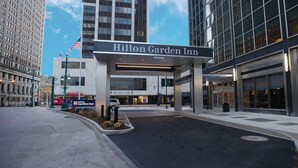 The exterior of the Hilton Garden Inn, featuring a prominent entrance with a large sign, a flag, and a well-maintained sidewalk. - Hilton Garden Inn Buffalo Downtown (Buffalo)