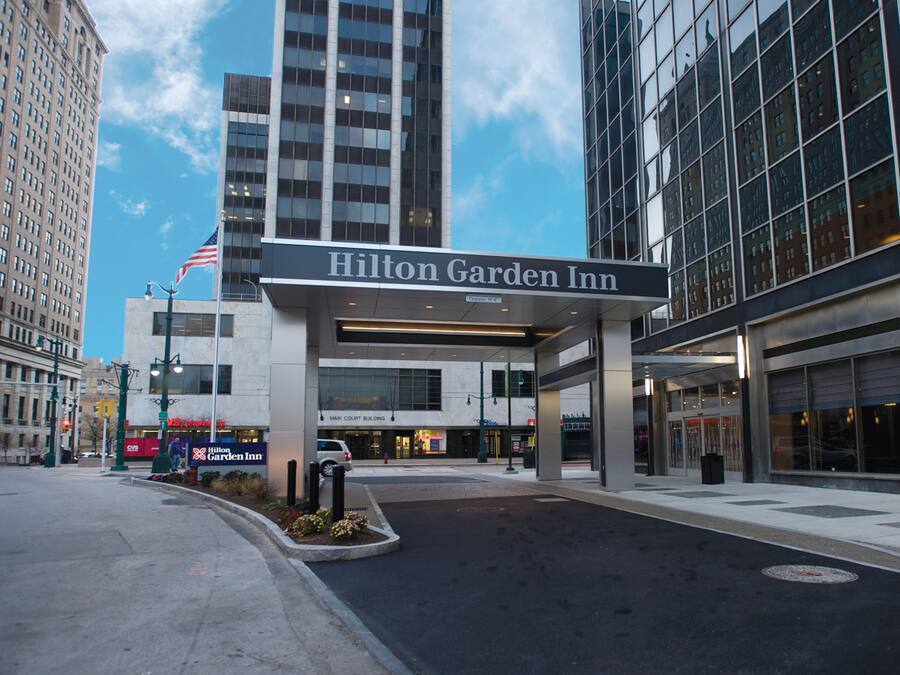 The exterior of the Hilton Garden Inn, featuring a prominent entrance with a large sign, a flag, and a well-maintained sidewalk.
