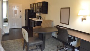 Habitación de hotel compacta con kitchenette, zona de comedor con mesa y sillas, y pequeño espacio de trabajo con escritorio y silla.
