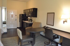 Habitación de hotel compacta con kitchenette, zona de comedor con mesa y sillas, y pequeño espacio de trabajo con escritorio y silla.