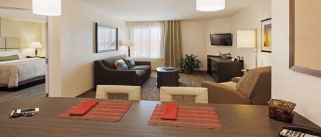 Habitación de hotel con una cama, dos sofás, una mesa de comedor con individuales, un televisor y un escritorio con teléfono.