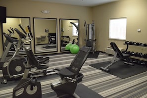 Un gimnasio con equipo de ejercicio, espejos y un ventanal.