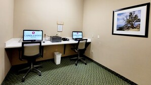 Una habitación de hotel con dos escritorios, cada uno con una computadora que muestra 'CANDLEWOOD SUITES'. Hay un cuadro en la pared y un cubo de basura en el suelo.